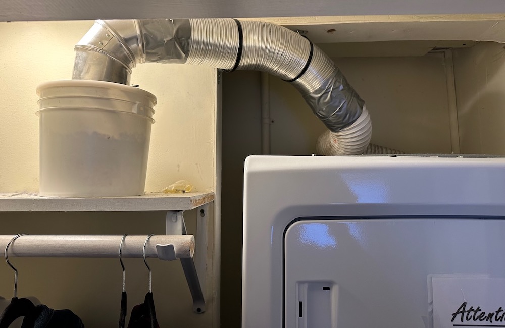 A clothes dryer vented to a bucket in the closet